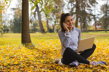 Young female sitting cross-legged on grass with laptop and talki