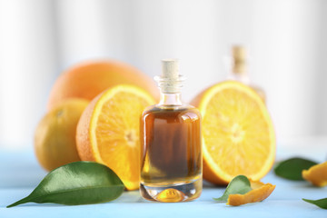 Bottle with essential oil, oranges and leaves on blue table