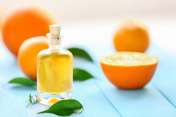 Bottle with essential oil, oranges and leaves on blue table