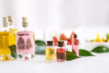 Bottles with essential oil and leaves on wooden table