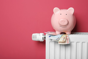 Fototapeta premium Savings concept. Piggy bank and money on heating radiator with temperature regulator on pink background