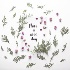 Inscription "HAVE A NICE DAY" written on paper with flowers on white background