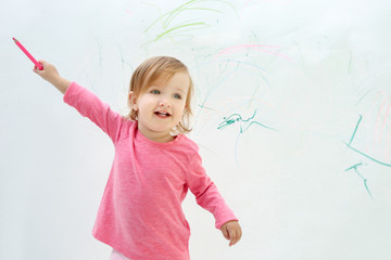 Cute little girl drawing on light wall