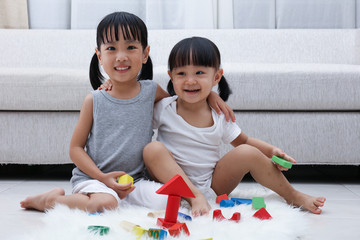 Happy Asian Chinese little sisters playing blocks on the floor