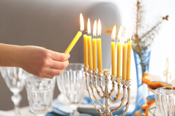 Female hand lighting candles in menorah on table served for Hanukkah