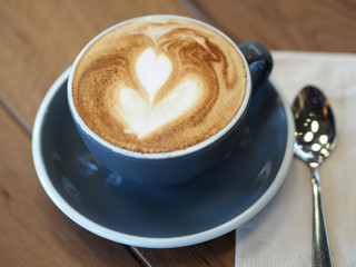 Cappuccino coffee in black cup on wooden table.