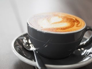 Cappuccino coffee in black cup on wooden table.