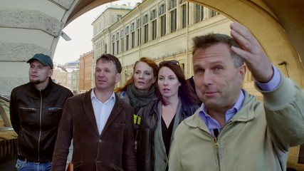 Tourist group with guide come close to the camera and look at the object behind. Background of old building with arch