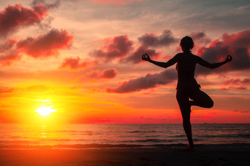 Fototapeta premium Silhouette young woman practicing yoga on the beach at surrealistic bloody red sunset.