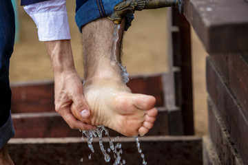 Male washing his feet on the sand beach. Place for washing the feet is made of wooden planks. Summer vacation at the seaside resort.