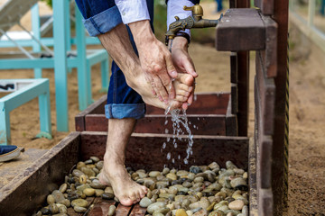 Man washing his feet on the sand beach. Place for washing the feet is made of wooden planks. The flooring is strewn with pebbles. Summer vacation at the seaside resort.