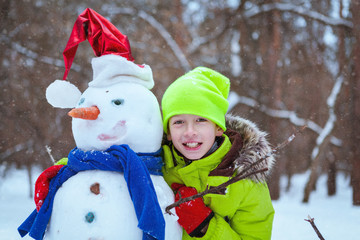 fun, happy kid playing with snowman in winter park