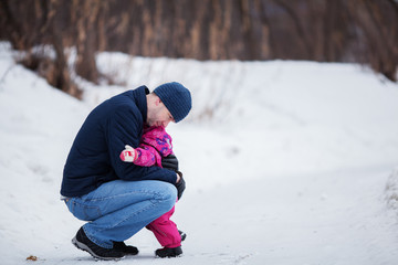 Fototapeta na wymiar Happy father walking with pretty beautiful little girl in winter park