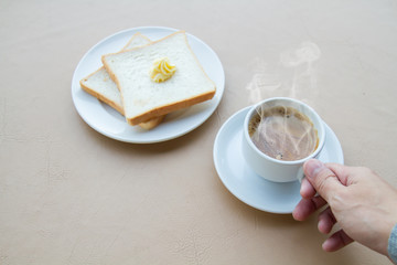 Hand holding coffee cup with toast and butter with copy space.