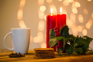 Lovely close up image of Christmas cookies on a wooden chopping board with some scented candles and a glass of whiskey / coffee and some cinnamon sticks.