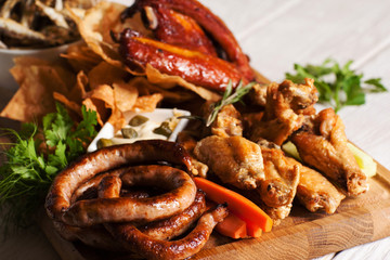 Assortment of grilled beer snacks close-up. Served on wooden board variety of smoked meals with creamy sauce. American cuisine, junk food, fat concept