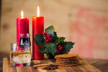 Lovely close up image of Christmas cookies on a wooden chopping board with some scented candles and a glass of whiskey / coffee and some cinnamon sticks.
