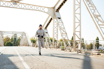 Concentrated sports man jogging across the bridge in the morning