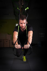 Fototapeta na wymiar One young handsome brave curly bearded muscled man with a beard makes Total Resistance eXercises fitness trx straps working out in gym crossfit