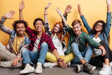 Cheerful young people sitting with raised hands and having fun