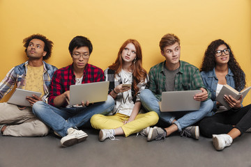 Multiethnic group of pensive young friends using laptops and thinking