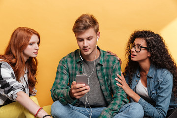 Two women sitting with man listening to music from smartphone