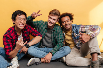 Three smiling men friends showing thumbs up and peace gestures