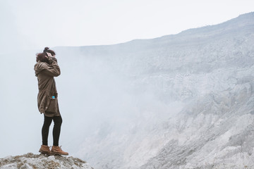 Female traveler standing on edge of mountain in Kawah Ijen volcano valley