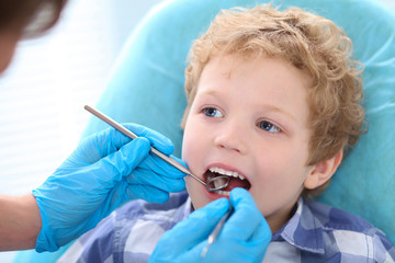 Male dentist examining a little boys teeth at the dental clinic.