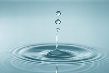 Water drop falling and drips on water mirror. Drops splash and make perfect circles on water surface