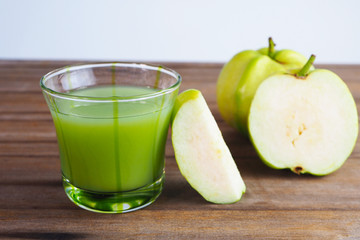 Close up of a healthy glass of fresh guava juice and fresh guava on a wooden table.