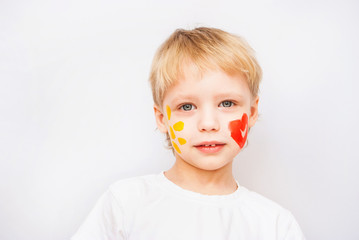 Portrait of funny beautiful blond child isolated on white background. Read heart and yellow sun on cheeks of boy.