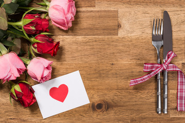 Flowers, silverware, greeting card on wooden table. Valentines day background