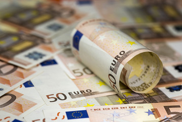 Half rolled hundred euro banknote lying on  fifty euro banknotes background