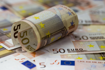 Half rolled fifty euro banknote lying on  fifty euro banknotes background