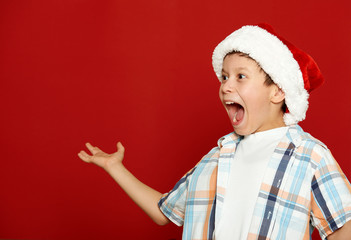 boy child portrait in santa hat on red, having fun and emotions, winter holiday concept