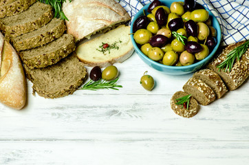 Fresh organic olives placed with ciabatta bread and whole grain brown bread and rosemary on white wooden background.Top view.Clean food concept.