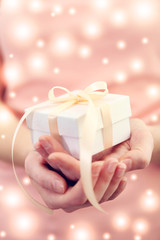 Female hands holding Christmas gift, closeup. Snowy effect