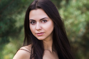 Graceful charming brunette model posing in black dress in coniferous park