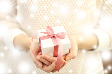 Female hands holding Christmas gift, closeup. Snowy effect