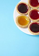 A plate full of assorted fruit jam tarts on a bright blue background with blank space below