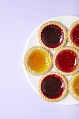 Aerial view of a plate full of assorted fruit jam tarts on a pastel purple background