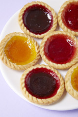 A plate full of assorted fruit jam tarts on a pastel purple background