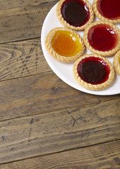 A plate full of assorted fruit jam tarts on a rustic wooden table top background with blank space below