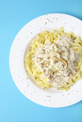 Overhead view of a dinner dish full of tagliatelle spaghetti with a creamy mushroom pasta sauce, on a bright blue background