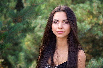 Naklejka premium Graceful charming brunette model posing in black dress in coniferous park