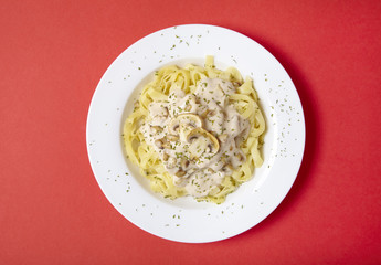 Aerial view of a dinner dish full of tagliatelle spaghetti with a creamy mushroom pasta sauce, on a bright red background