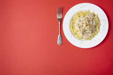 A dinner dish full of tagliatelle spaghetti with a creamy mushroom pasta sauce, on a bright red background with fork and empty space at side