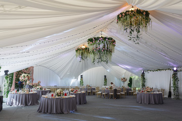 Chandeliers made of roses and greenery hang under the white tent
