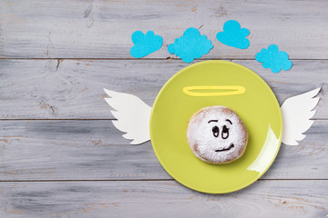 Donut with smiley face angel on a plate, wooden background